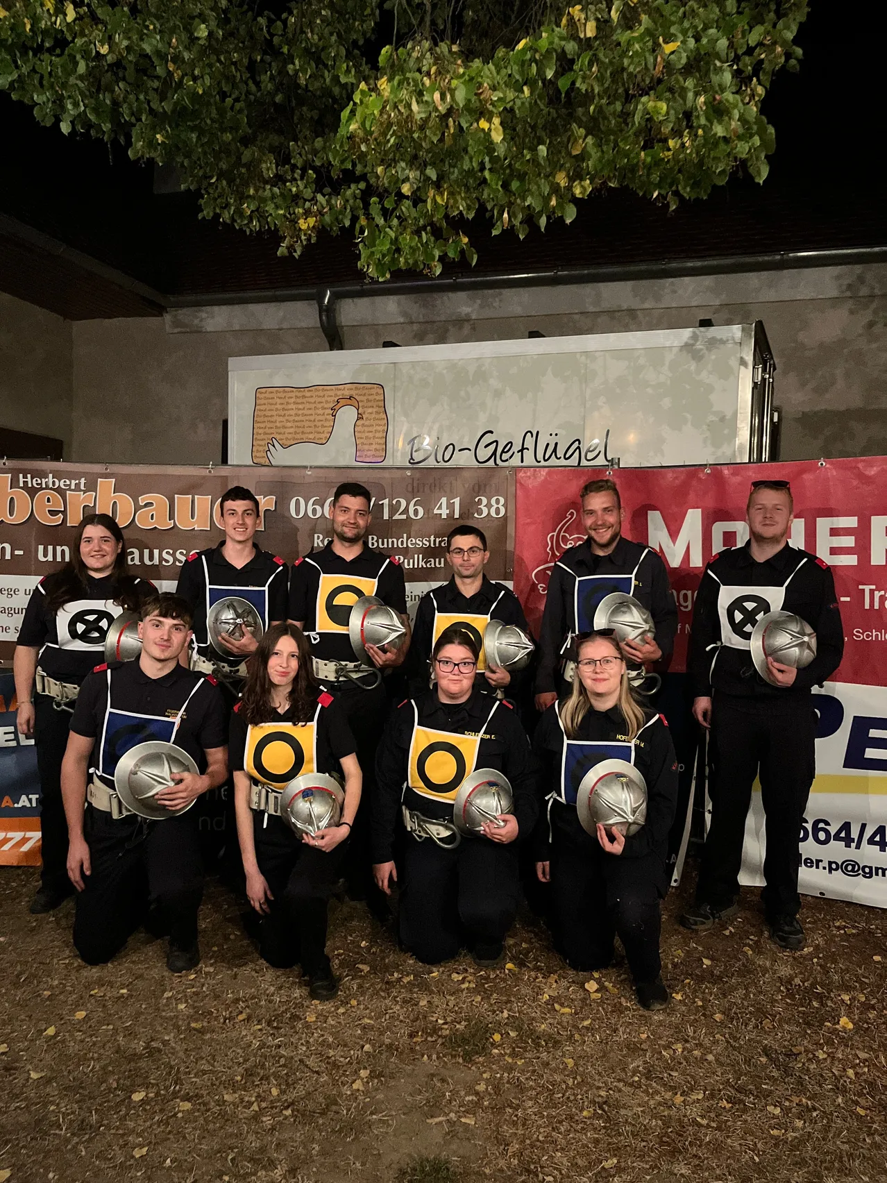 Eine Gruppe von Menschen in schwarzen Uniformen mit gelben und weißen Designs posiert für ein Foto mit silbernen Helmen in den Händen.