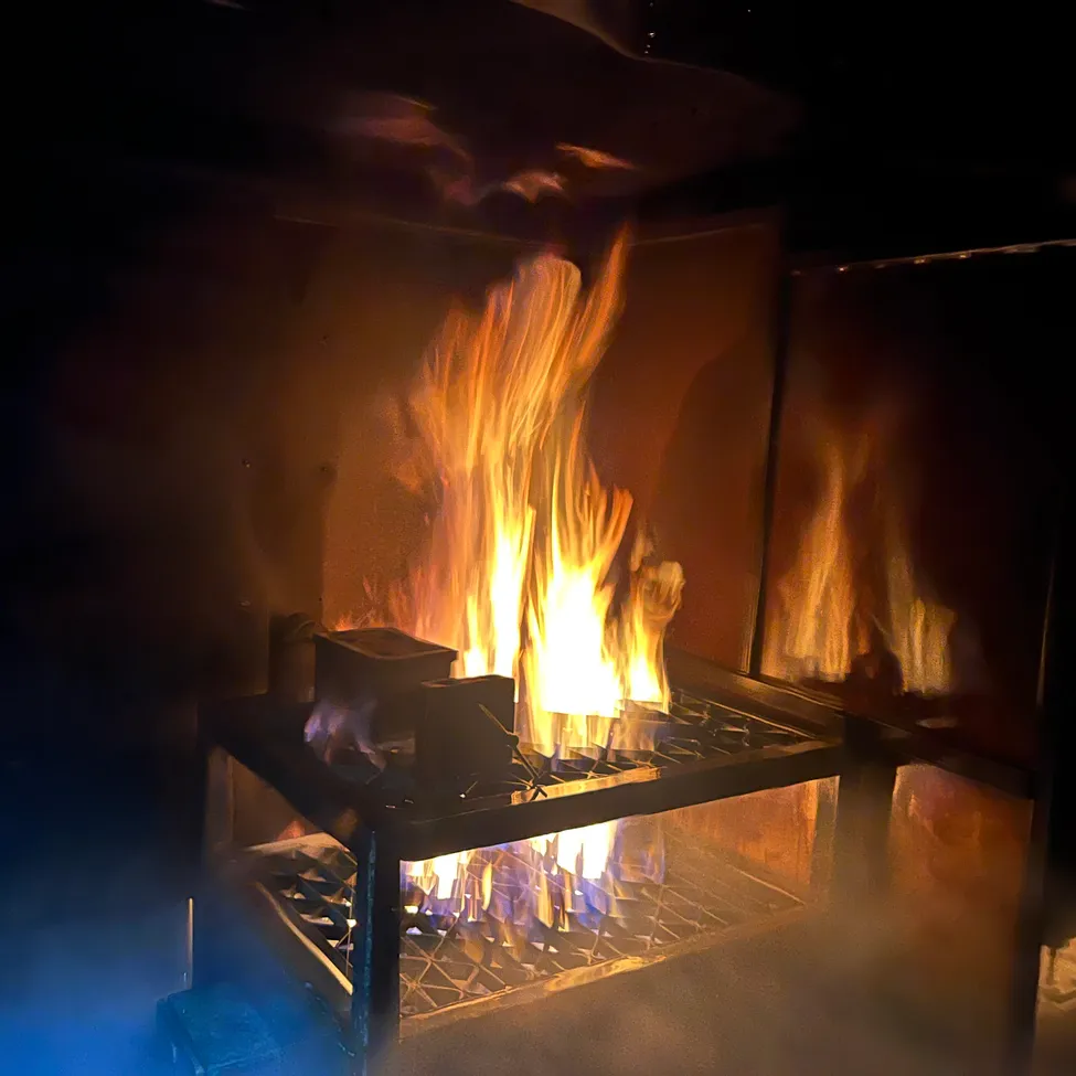Ein Kamin mit einem hell brennenden Feuer, das warmes Licht und Schatten im Raum wirft.
