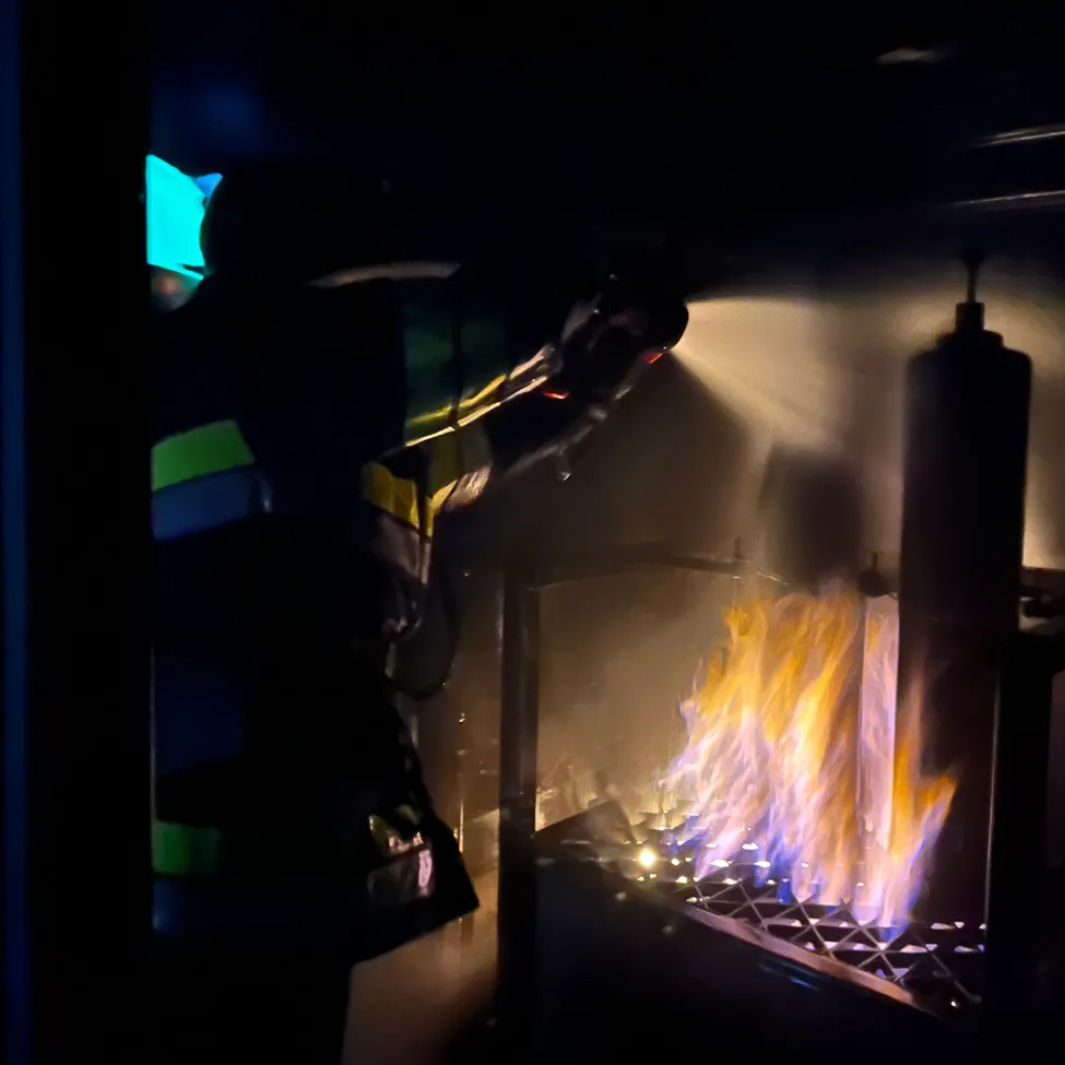 Ein Feuerwehrmann spritzt Wasser auf ein Feuer in einem dunklen Raum.