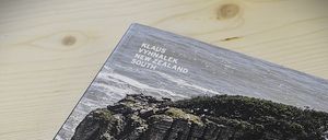 Ein Foto eines rauen Klippen mit dem Text 'KLAUS VYHNALEK NEW ZEALAND SOUTH' auf dem Cover, auf einer Holzoberfläche angezeigt.