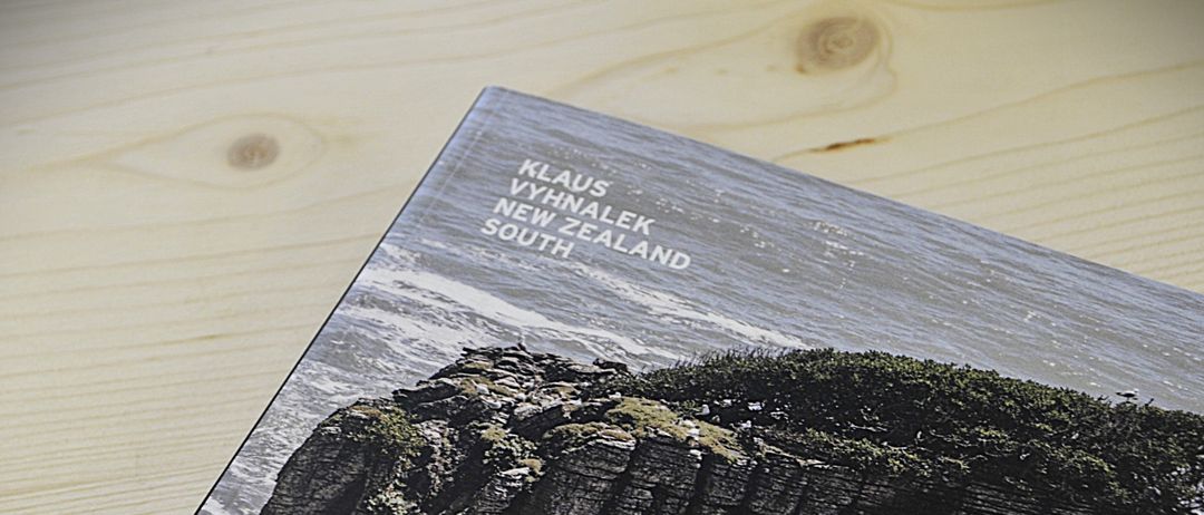 Ein Foto eines rauen Klippen mit dem Text 'KLAUS VYHNALEK NEW ZEALAND SOUTH' auf dem Cover, auf einer Holzoberfläche angezeigt.