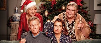 Filmplakat zeigt vier Menschen auf einer Couch, zwei Frauen in Rot und einen Mann in Grau. Sie lächeln und posieren für ein Foto. Der Weihnachtsbaum steht hinter ihnen.