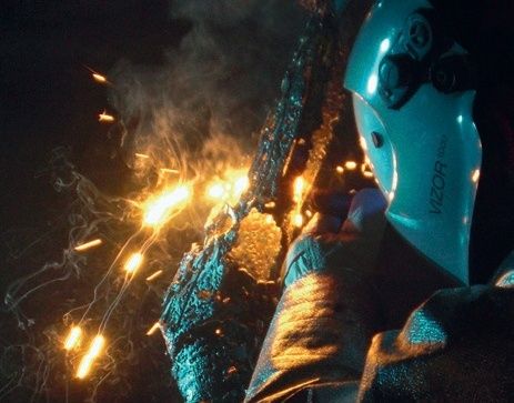 Ein Schweißer arbeitet an einem glühenden Metallstück mit fliegenden Funken in einem schwach beleuchteten Bereich.