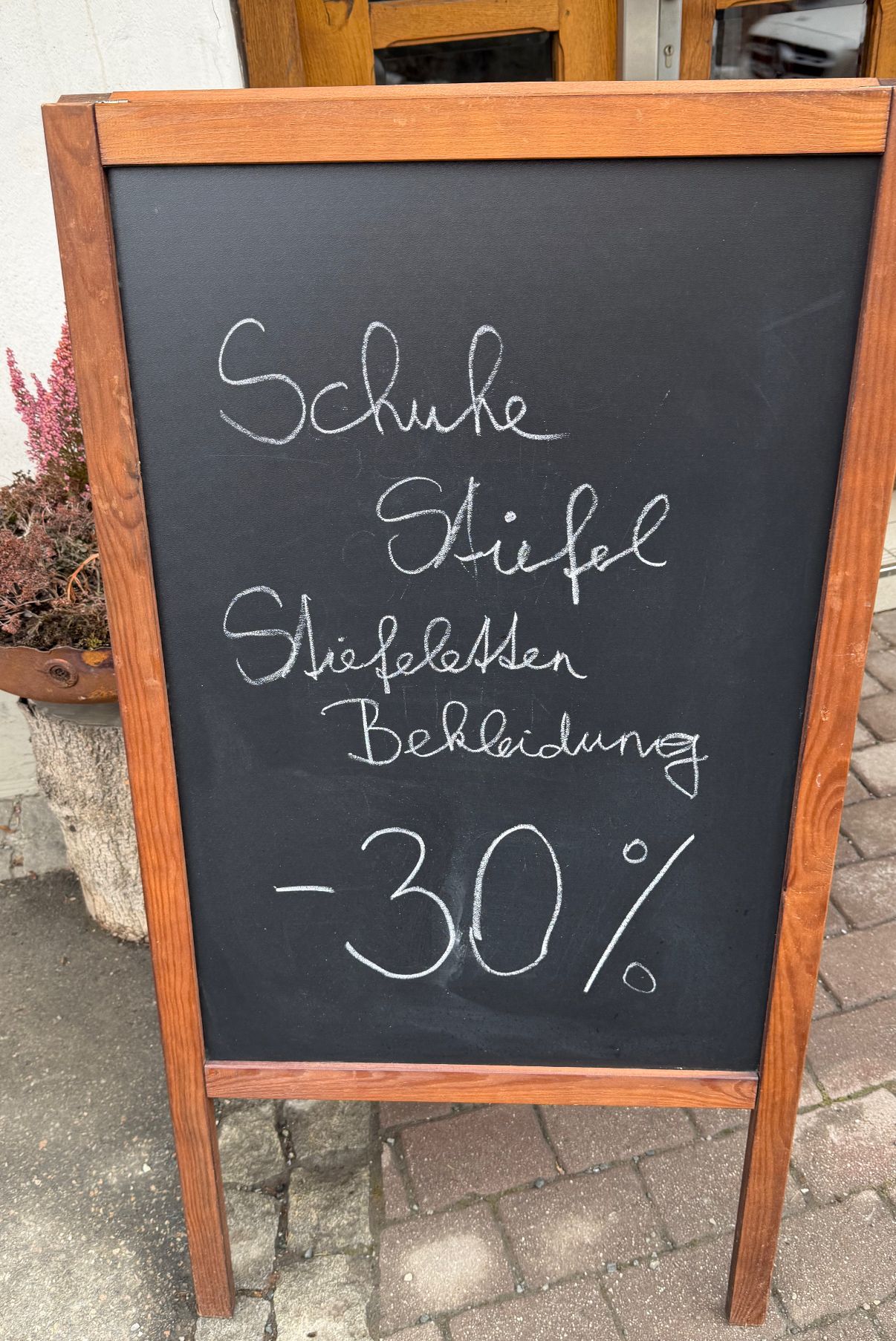 A blackboard with a list of items on sale. The items include Schuke Stiefel, Schiefelessen, and Bekleidung. The discount is 30% off.