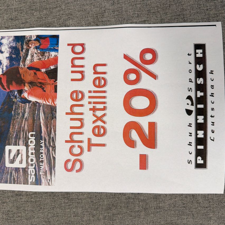 Ein Werbeplakat für PINNITSCH Schuhsport mit einem Rabatt von 20% auf Schuhe und Textilien. Das Plakat zeigt eine Person in einer roten Jacke beim Bergsteigen.