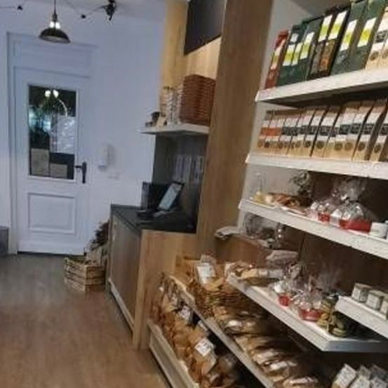 Innenansicht eines Ladens mit Holzregalen, Lebensmitteln, einer weißen Tür und einer Theke.