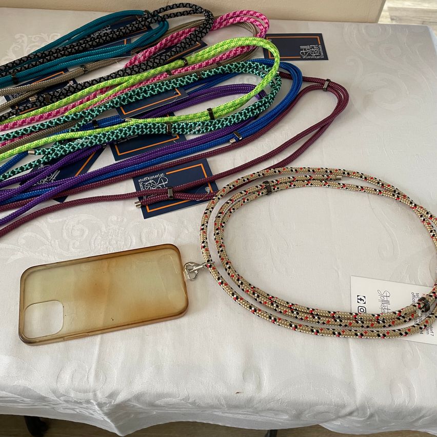 Eine Sammlung bunter geflochtener Gurte und eine iPhone-Hülle sind auf einem weißen Tuch ausgelegt.