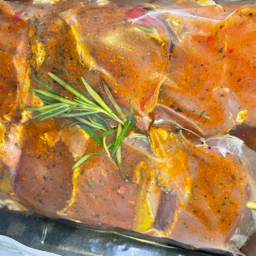 Ein Nahaufnahme von mariniertem Fleisch in einer Plastiktüte, gekrönt von einem Rosmarinzweig. Das Fleisch ist mit einer Mischung aus Kräutern und Gewürzen überzogen.