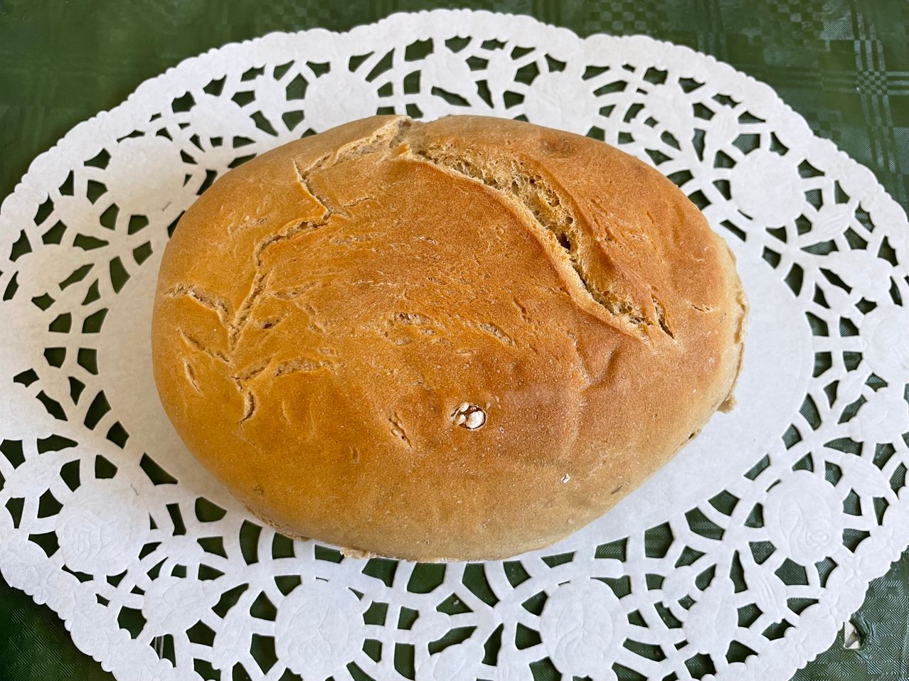 Ein Laib Brot mit leicht geplatzter Kruste liegt auf einem weißen Doily mit grünem Hintergrund.