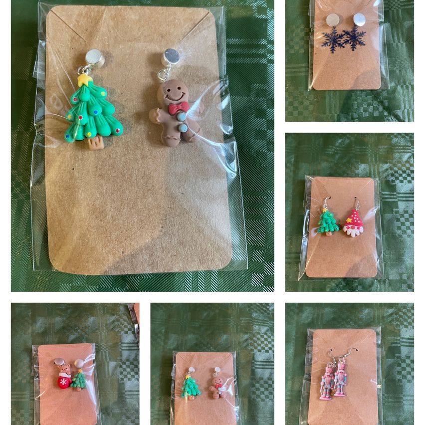 Eine Sammlung von weihnachtlich gestalteten Ohrringen, darunter ein Lebkuchenmann, ein Weihnachtsbaum und eine Nussknacker, jeweils einzeln in Klarsichtfolie verpackt und auf braunem Papier präsentiert.