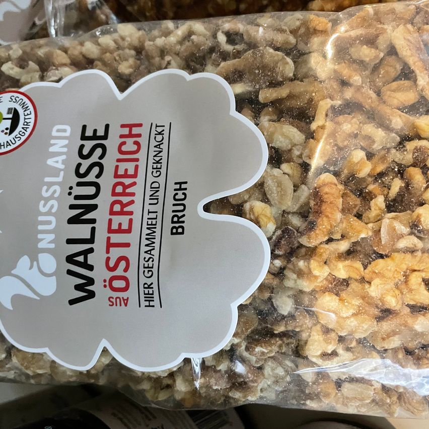 Ein Beutel mit zerkleinerten Walnüssen, beschriftet mit 'Walnuesse Osterreich', von Nussland, vor einem unscharfen Hintergrund.