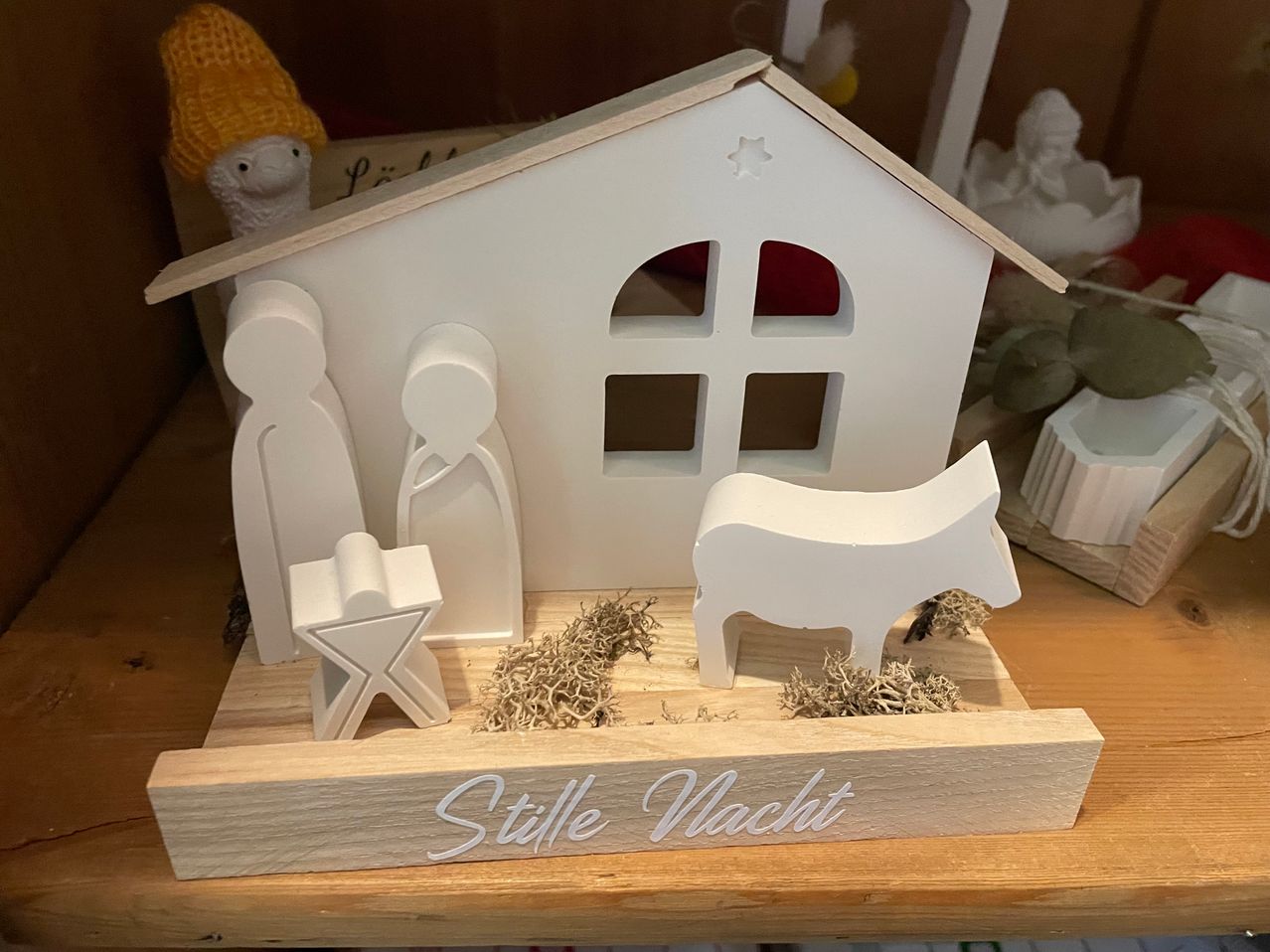 Eine kleine hölzerne Krippe auf einem Holzsockel, mit Figuren von Maria, Josef und Jesus, einem Stern und einem Ochsen. Der Sockel trägt die Aufschrift 'Stille Wacht'.