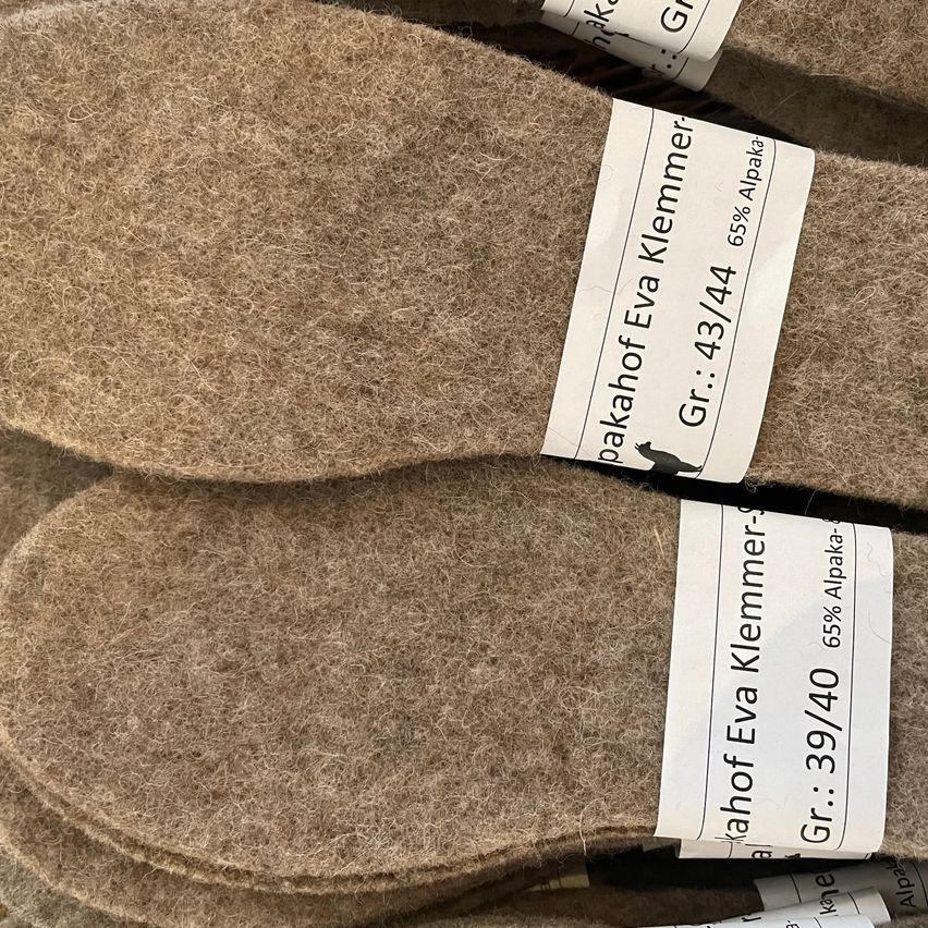 Mehrere Paare brauner Wolleinlagen gestapelt. Jede hat einen Aufkleber mit 'Gr. 43/44', '65% Alpaka' und 'Eva Klemmer'. Das letzte Paar hat einen Aufkleber mit 'Gr. 39/40', '65% Alpaka'.