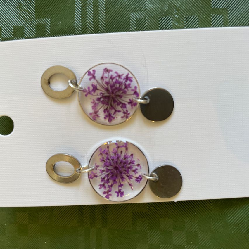 Two pairs of earrings with metal hoops and round charms. Each charm contains a preserved flower, one in purple and one in pink.