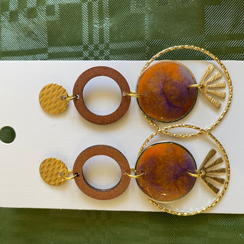 A set of golden and brown earrings with a sunburst design, showcasing orange and purple centers on a white background.