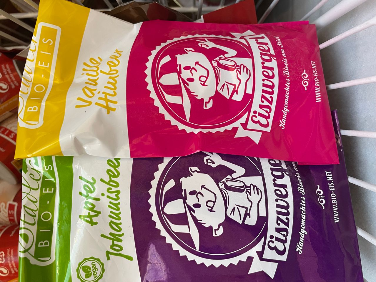 Two bags of chips stacked on top of each other, with one pink and one purple bag. Both bags have a cartoon character on them. The pink bag has vanilla flavor, and the purple bag has apple flavor.