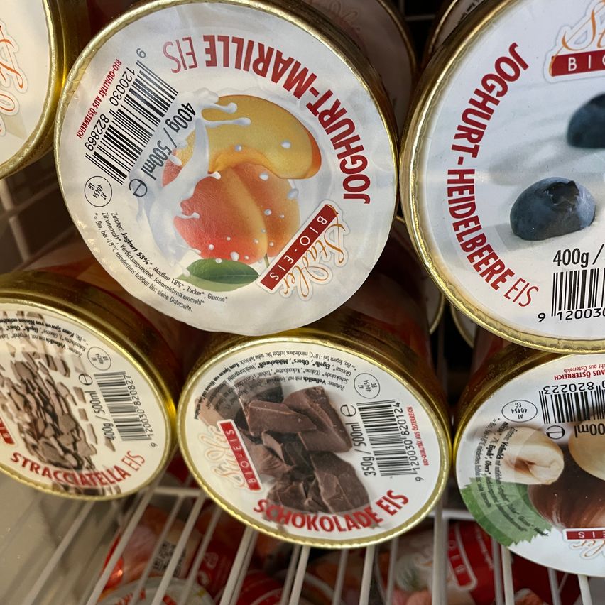 Four tins of ice cream, three with fruit and one with chocolate. Each tin has a gold lid and is on a white shelf.