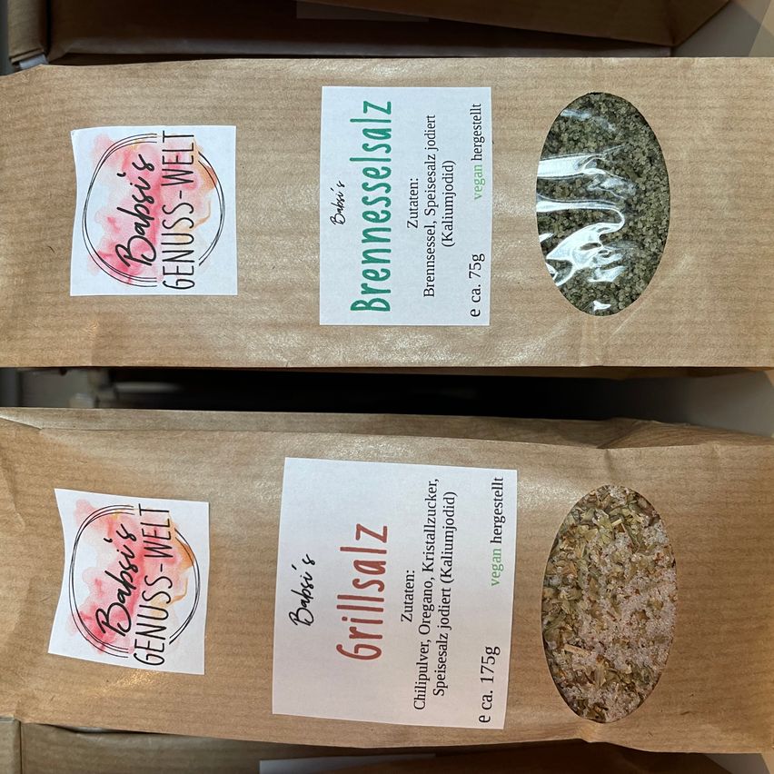 Zwei braune Gewürzbeutel, jeweils mit Etikett. Der obere ist mit 'Brenneselsalz' und der untere mit 'Grillsalz' beschriftet. Beide haben kleine Fenster, die den Inhalt zeigen.