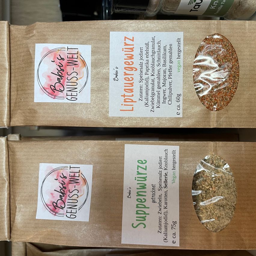 Zwei braune Papiertüten mit Etiketten. Die oberste trägt die Aufschrift 'Liptauergewürz' und die unterste 'Suppenwürze'. Beide haben ein transparentes Fenster, das den Inhalt zeigt.