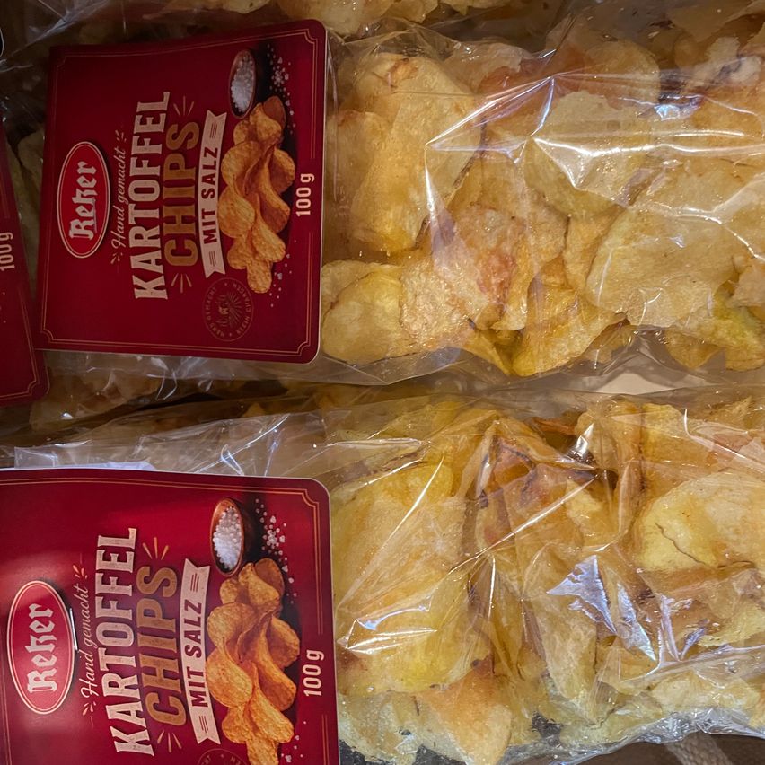 Zwei Tüten Kartoffelchips mit einem roten Etikett, das Kartoffel Chips mit Salz anzeigt. Die Chips sind in durchsichtigen Plastiktüten.