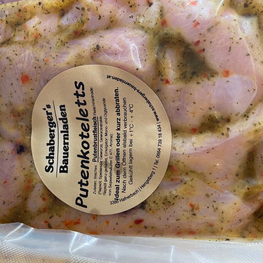 Ein Nahaufnahme von marinierten Hühnchenschenkeln in Plastikverpackung mit einem Etikett, das 'Putenkötelettes' lautet. Das Huhn ist mit Kräutern und Gewürzen gewürzt.