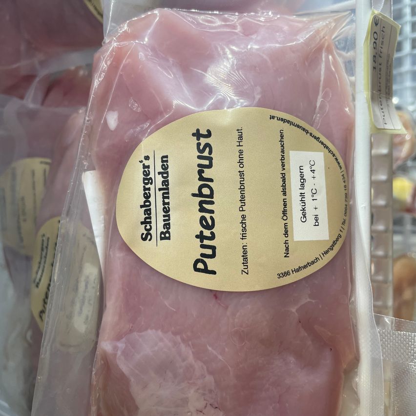 Eine Packung rohen Schweinefleischs, gekennzeichnet als Putenbrust, zeigt an, dass es sich um frische Putenbrust von einem Bauernhof in Deutschland handelt. Die Packung ist mit einem gelben Etikett versiegelt und in einem Kühlschrank aufbewahrt.