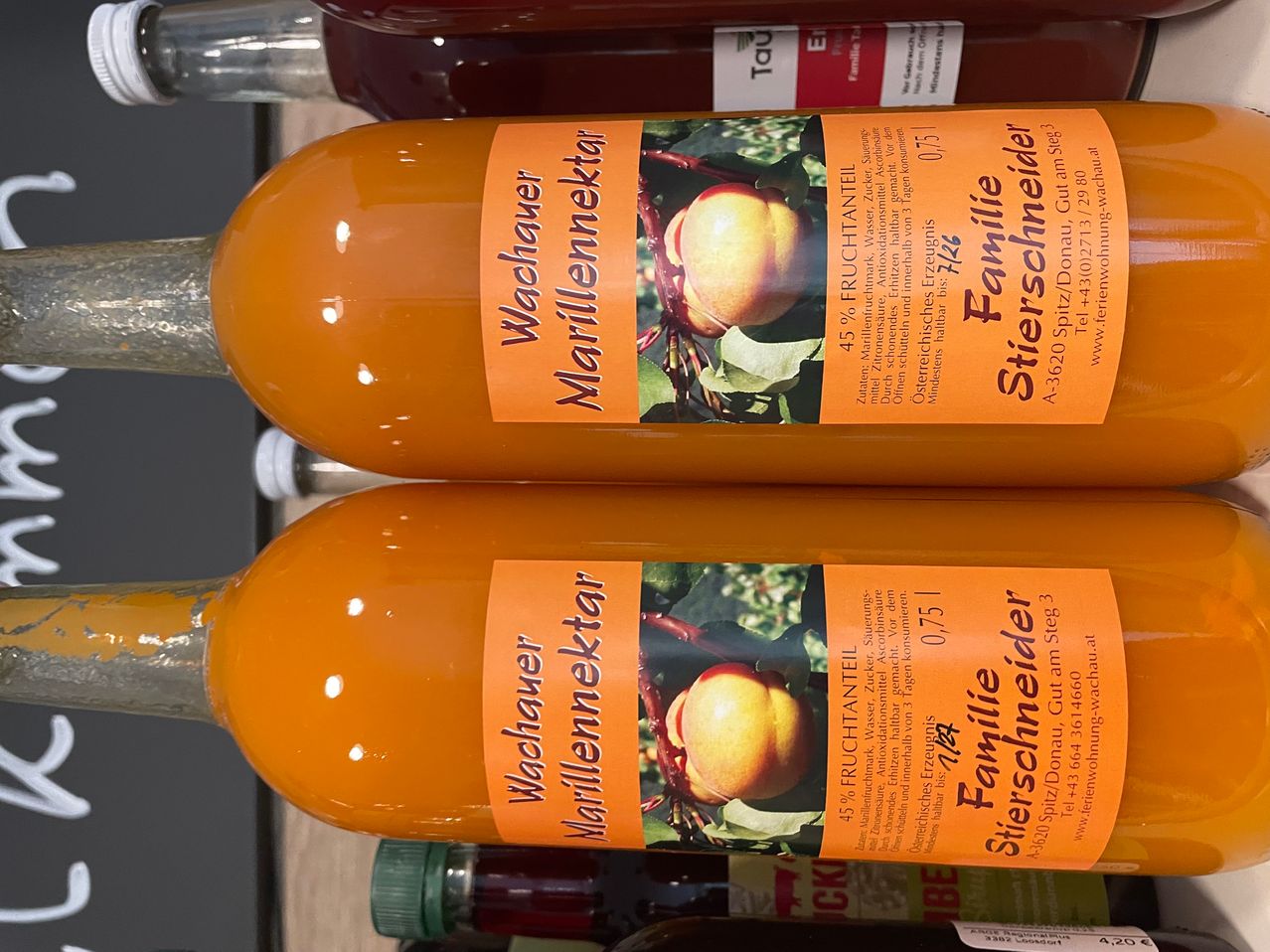 Zwei Flaschen Wachauer Marillennektar mit orangefarbenen Etiketten, die einen Pfirsich auf einem Zweig zeigen. Das Etikett enthält Angaben zum Fruchtgehalt und Lagerungsempfehlungen.
