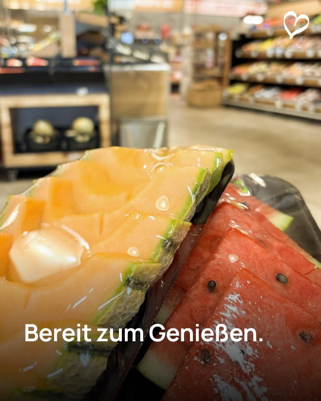Ein Nahaufnahme eines verpackten Cantaloupe und einer Wassermelone in einem Supermarkt, mit Regalen im Hintergrund.