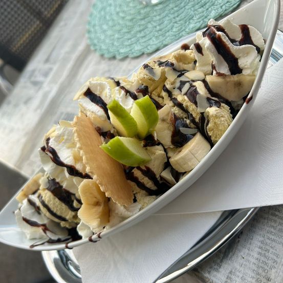 Eine weiße Schüssel mit Eiscreme, Bananen, Schlagsahne und Schokoladensauce auf einem Tisch mit einer Zeitung.