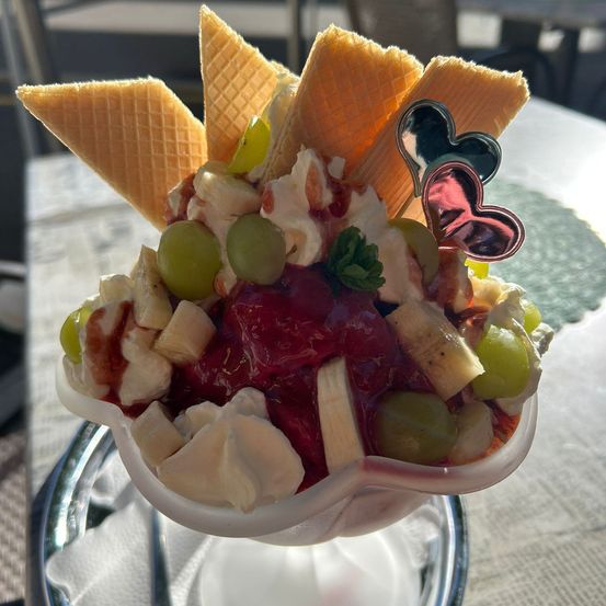 Eine Schüssel Eiscreme mit verschiedenen Früchten und Schlagsahne, gekrönt mit Waffelkegeln und herzförmigen Dekorationen.