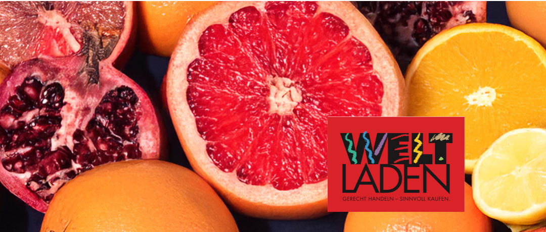 Ein Nahaufnahme eines roten Grapefruit-Schnittes mit anderen Früchten, darunter Orangen und Granatäpfel, im Hintergrund. Das Logo 'Welt Laden' ist unten rechts sichtbar.