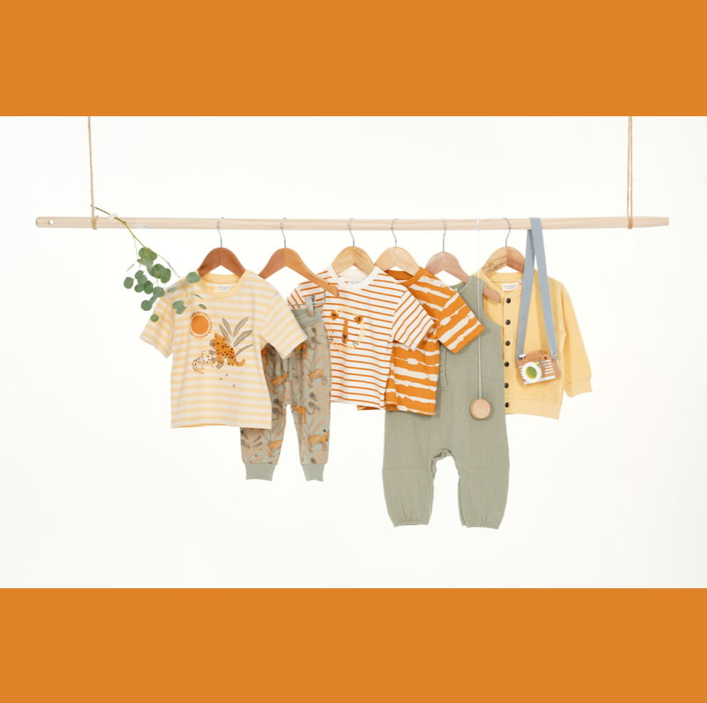 Five baby outfits are hanging on a wooden bar. The outfits include a shirt, pants, and a cardigan. They are colorful and have different designs.