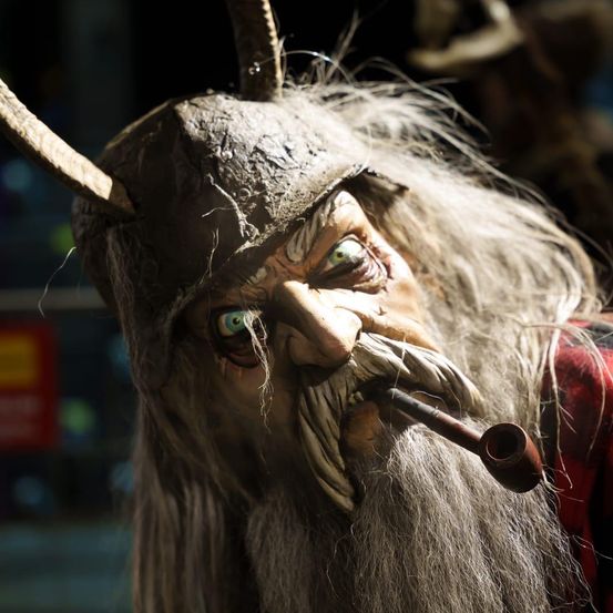 Ein Nahaufnahme von einem Mann, der eine Wikinger-ähnliche Kostüm trägt, mit einer Pfeife im Mund und Hörnern auf dem Kopf. Der Mann hat einen Bart und langes weißes Haar.