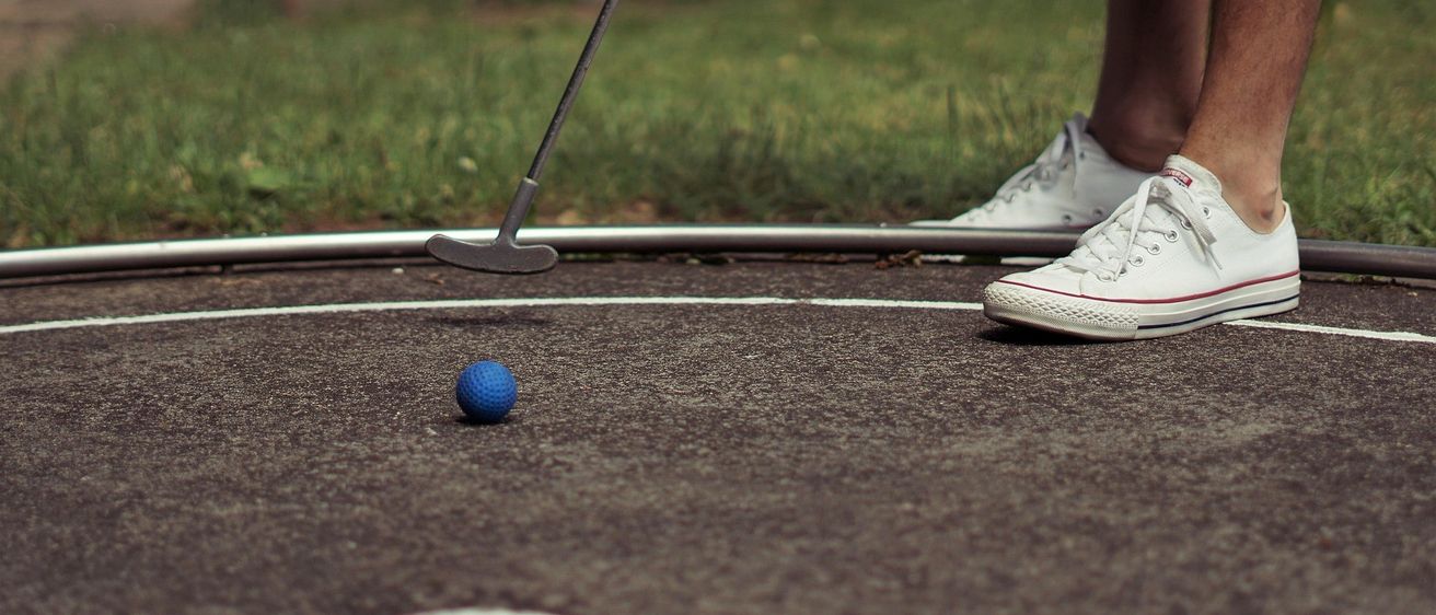 Ein Golfspieler steht auf einem Platz und bereitet sich darauf vor, einen blauen Ball in Richtung Loch zu putten, mit weißen Schuhen und einem Putter sichtbar.