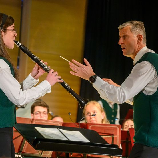 Eine junge Frau übt das Spielen der Klarinette mit einem Dirigenten vor einer Band.