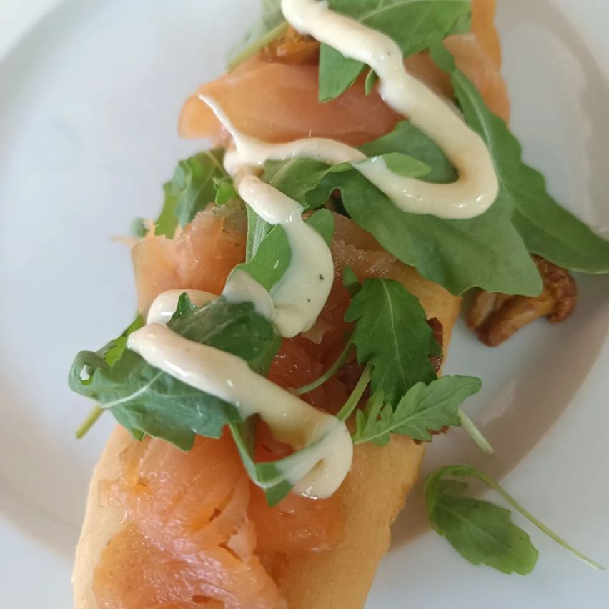 Ein Sandwich mit Räucherlachs, weißer Sauce und grünen Blättern auf einem weißen Teller.