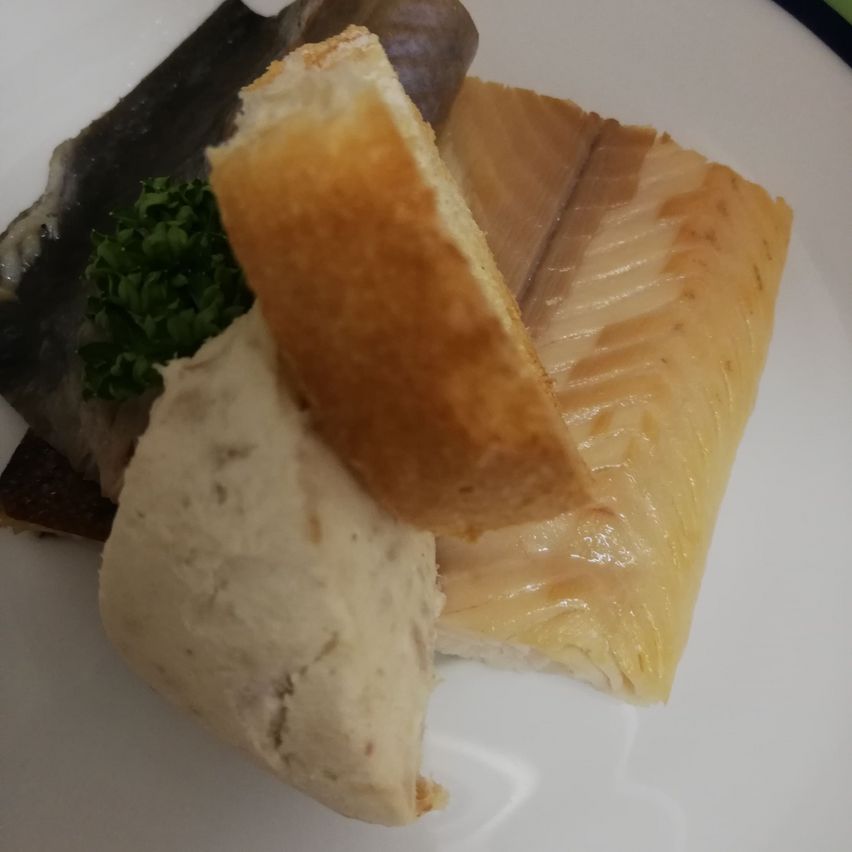Ein Teller mit geräuchertem Fisch, einer Scheibe Brot und einem Stück weißer Substanz, möglicherweise eine Dip, garniert mit grünen Kräutern.