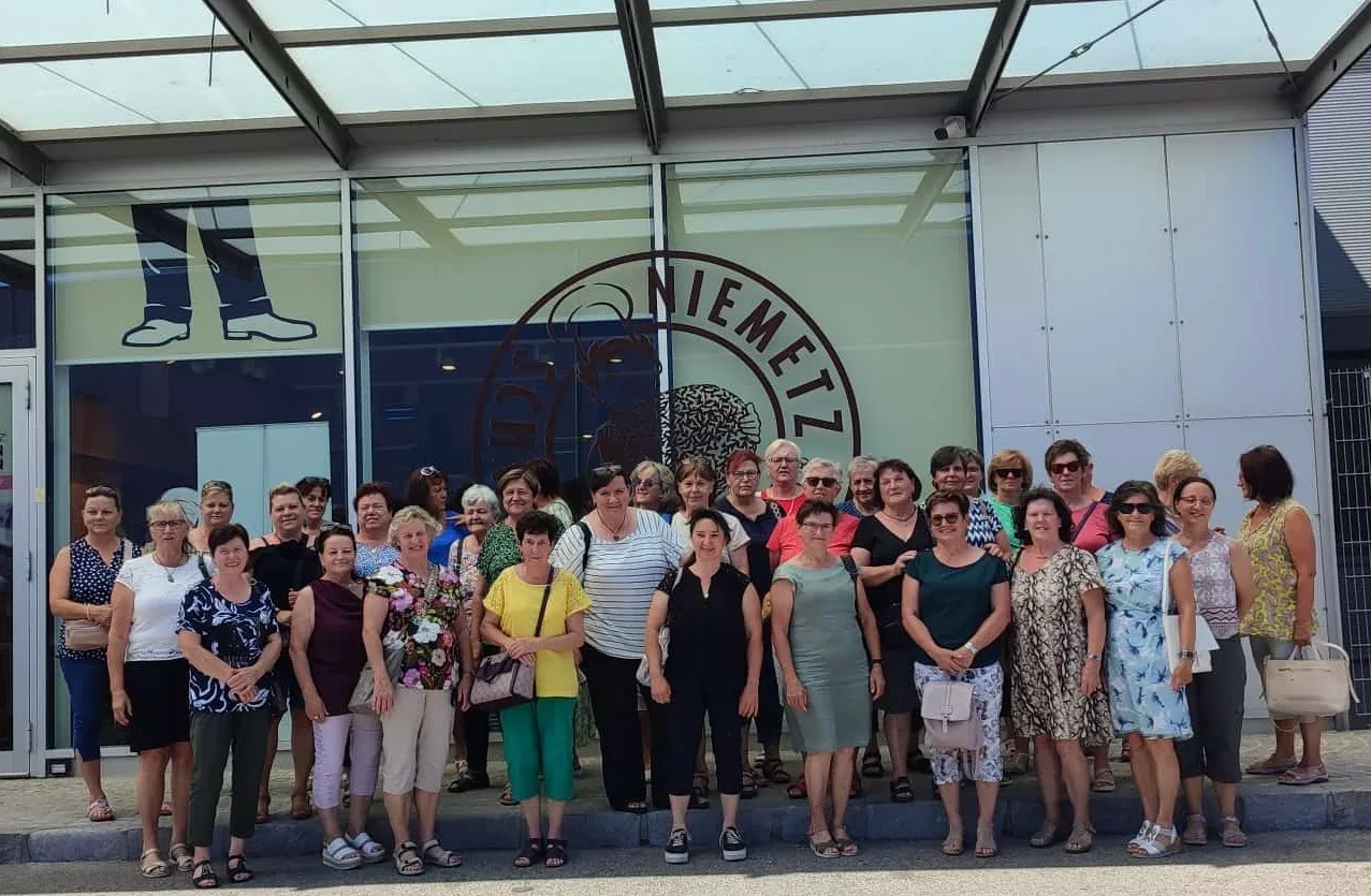 Eine Gruppe von Frauen, möglicherweise Touristen, posiert für ein Foto vor einem glasfrontigen Gebäude, möglicherweise einem Geschäft, mit einem Logo, das einen Gehirn und einen Kreis zeigt.