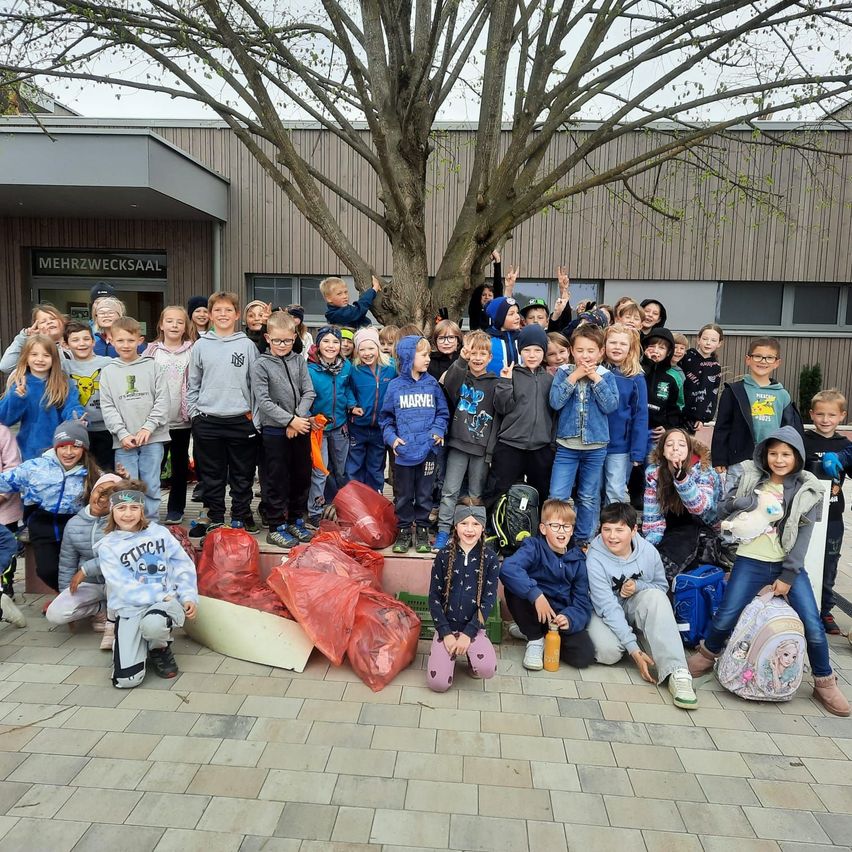 A large group of children poses for a photo in front of a building, with bags of trash nearby.