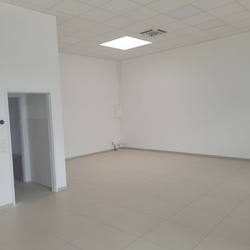 Ein leerer Raum mit weißen Wänden und beigefarbenen Fliesenböden. Es gibt eine Tür links und ein Licht an der Decke.