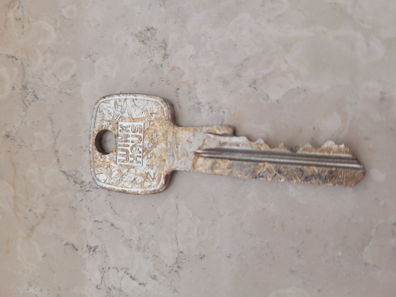 A gold-colored key with the word 'PLUS' engraved on it lies on a marble surface.