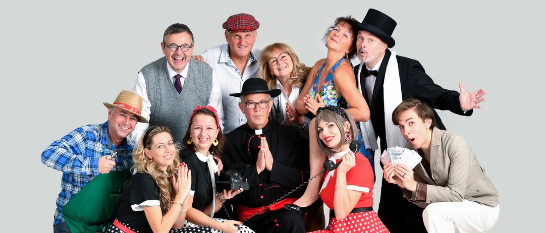 Eine Gruppe von Erwachsenen in Vintage-Kleidung und Hüten posiert für ein Foto, einige lächeln und halten Requisiten wie Telefone und Geld.