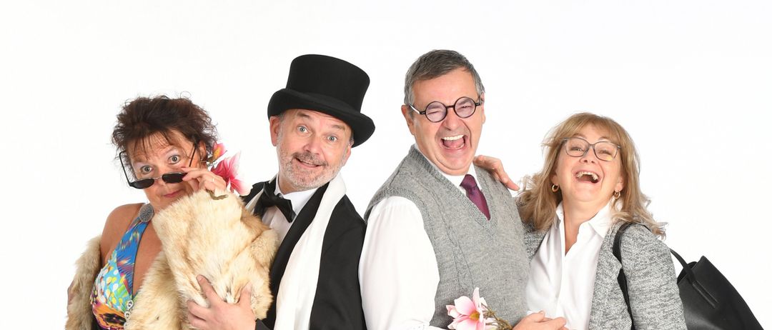 Vier Personen posieren für ein Foto. Die beiden Frauen tragen Pelzmäntel und Kleider, die beiden Männer formelle Kleidung. Sie alle lächeln.