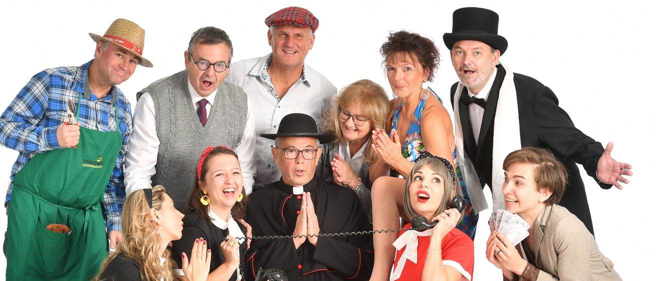 Eine Gruppe von Erwachsenen in verschiedenen Kostümen, einschließlich eines Priesters, posiert für ein Foto. Einige tragen Hüte, Brillen und Schmuck und sie alle lächeln und machen lustige Gesichter.