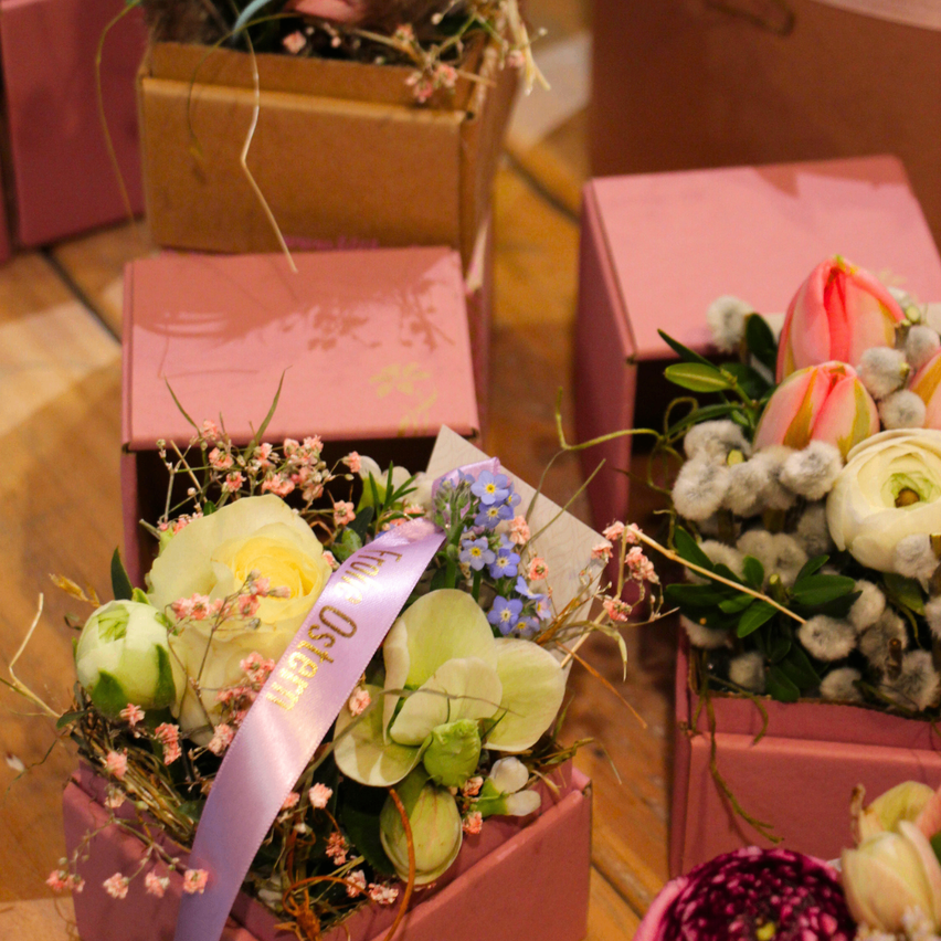 Mehrere rosafarbene Schachteln enthalten Blumenarrangements. Die Blumen sind weiß, rosa und blau. Eine lila Schleife mit dem Text 'Miss USA' ist um eines der Arrangements gebunden.
