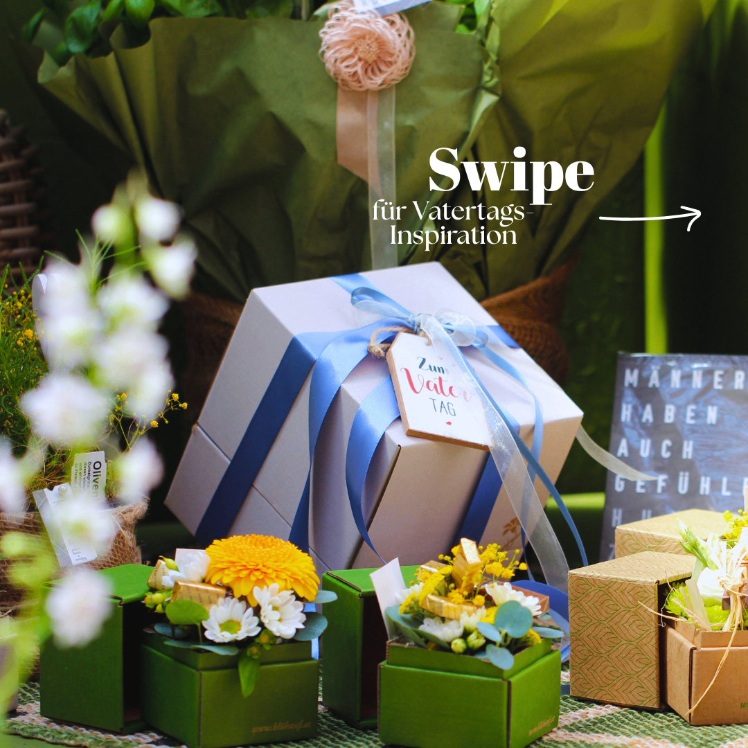 A large gift box with a blue ribbon and tag sits with several smaller green boxes. Flowers and plants are visible in the background.