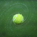 Ein Tennisball in der Luft, umgeben von Wassertropfen, die einen dynamischen und lebendigen Effekt erzeugen.