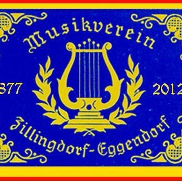 Blaues Abzeichen mit goldenem Design, das ein Lyre-Symbol, die Texte '1877', '2012' und 'Filndorf-Eggendorf' in goldener Schrift zeigt. Dekorative Elemente an den Rändern.