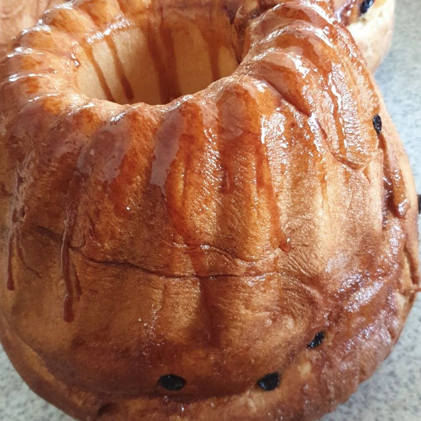 Ein Nahaufnahme eines glasierten Donuts mit karamellisierten Sirup, der an den Seiten heruntertropft. Der Donut hat eine goldbraune Farbe und steht auf einer Marmoroberfläche.