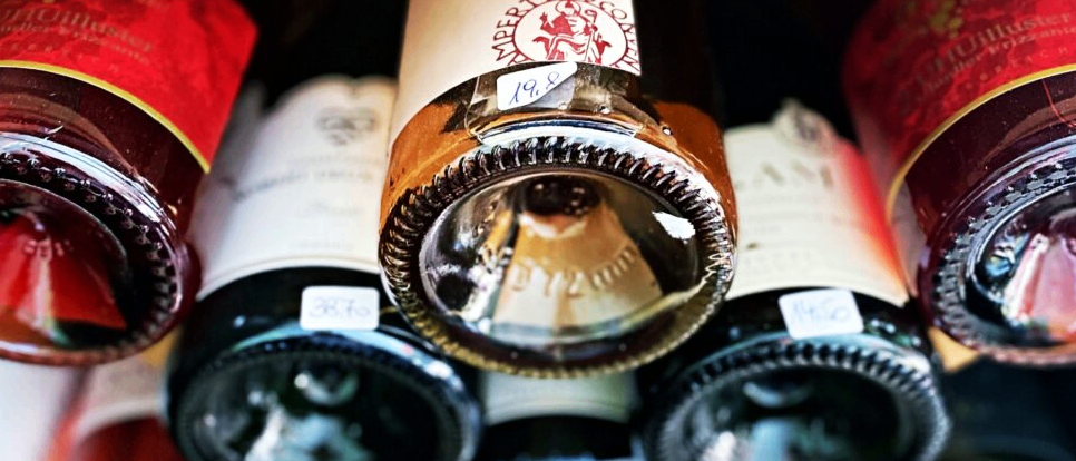 Eine Sammlung von Weinflaschen wird mit Fokus auf die mittlere Flasche gezeigt, wobei Korken und Etikett hervorgehoben sind. Die Flaschen sind vertikal gestapelt.